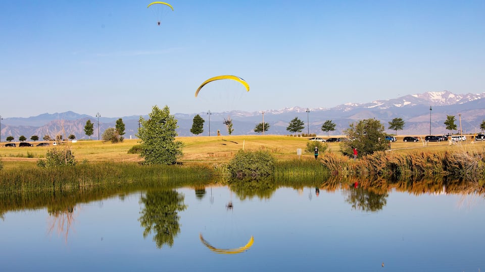 A calm lake with reflections of yellow parachutes and a mountainous landscape in the background.