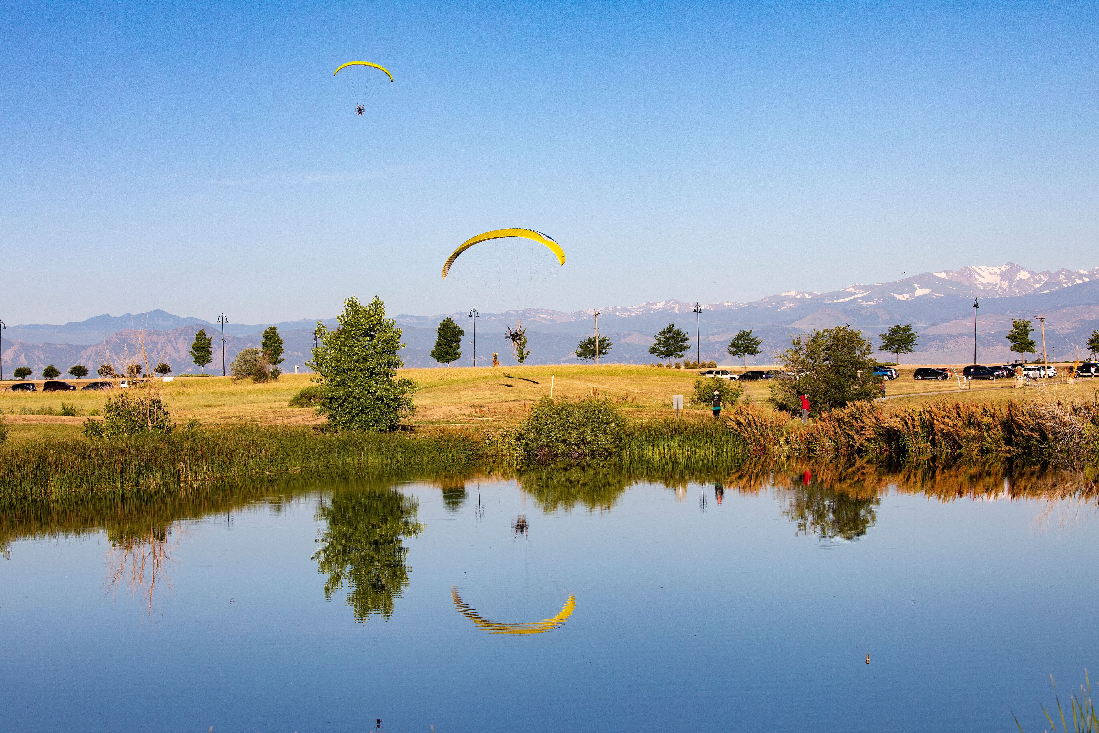 A calm lake with reflections of yellow parachutes and a mountainous landscape in the background.