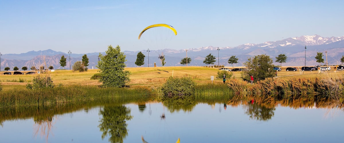 A calm lake with reflections of yellow parachutes and a mountainous landscape in the background.