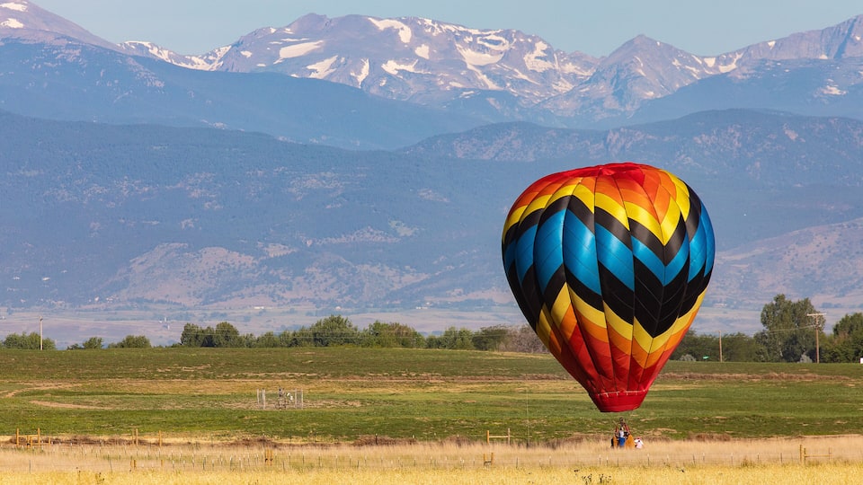 A colorful hot air balloon over a grassy field with snow-capped mountains in the background.
