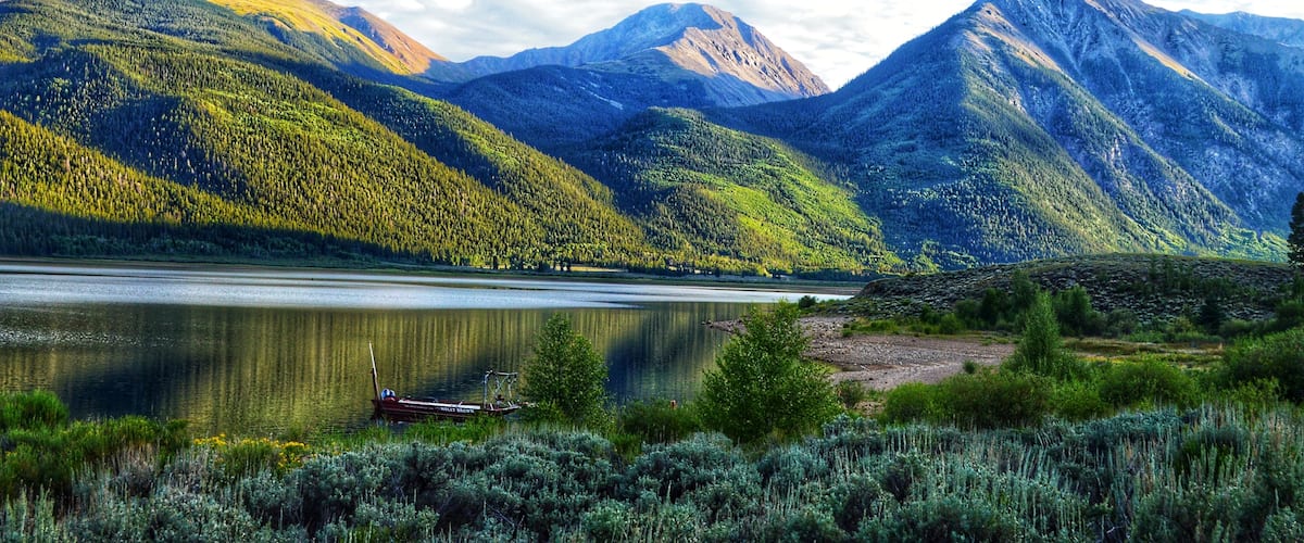 A lake surrounded by mountains, a boat on the water, and lush greenery.