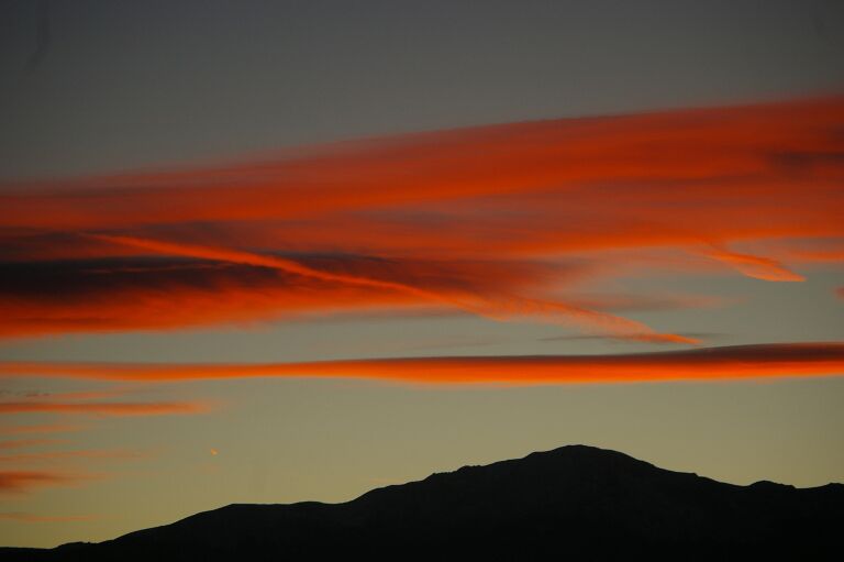 Um pôr do sol com nuvens vermelhas sobre uma cordilheira.