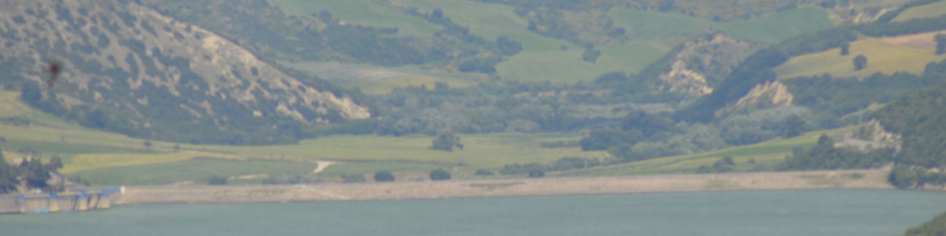 Paisagem costeira com colinas ondulantes, um corpo d'água e uma pequena ilha.