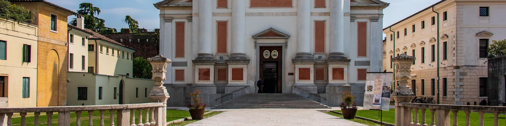 A historic building with statues on the roof, a plaque, and a well-maintained garden.