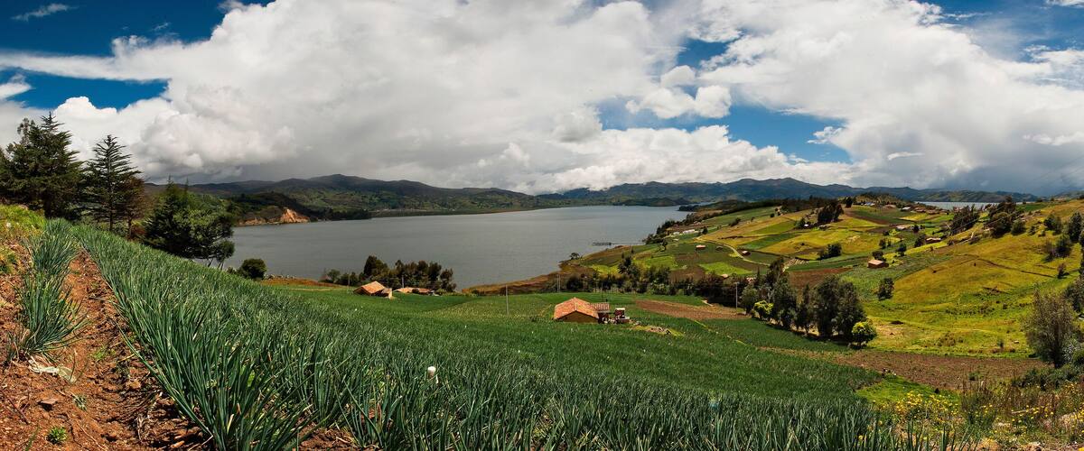 A lake surrounded by green fields, mountains, and a cloudy sky.