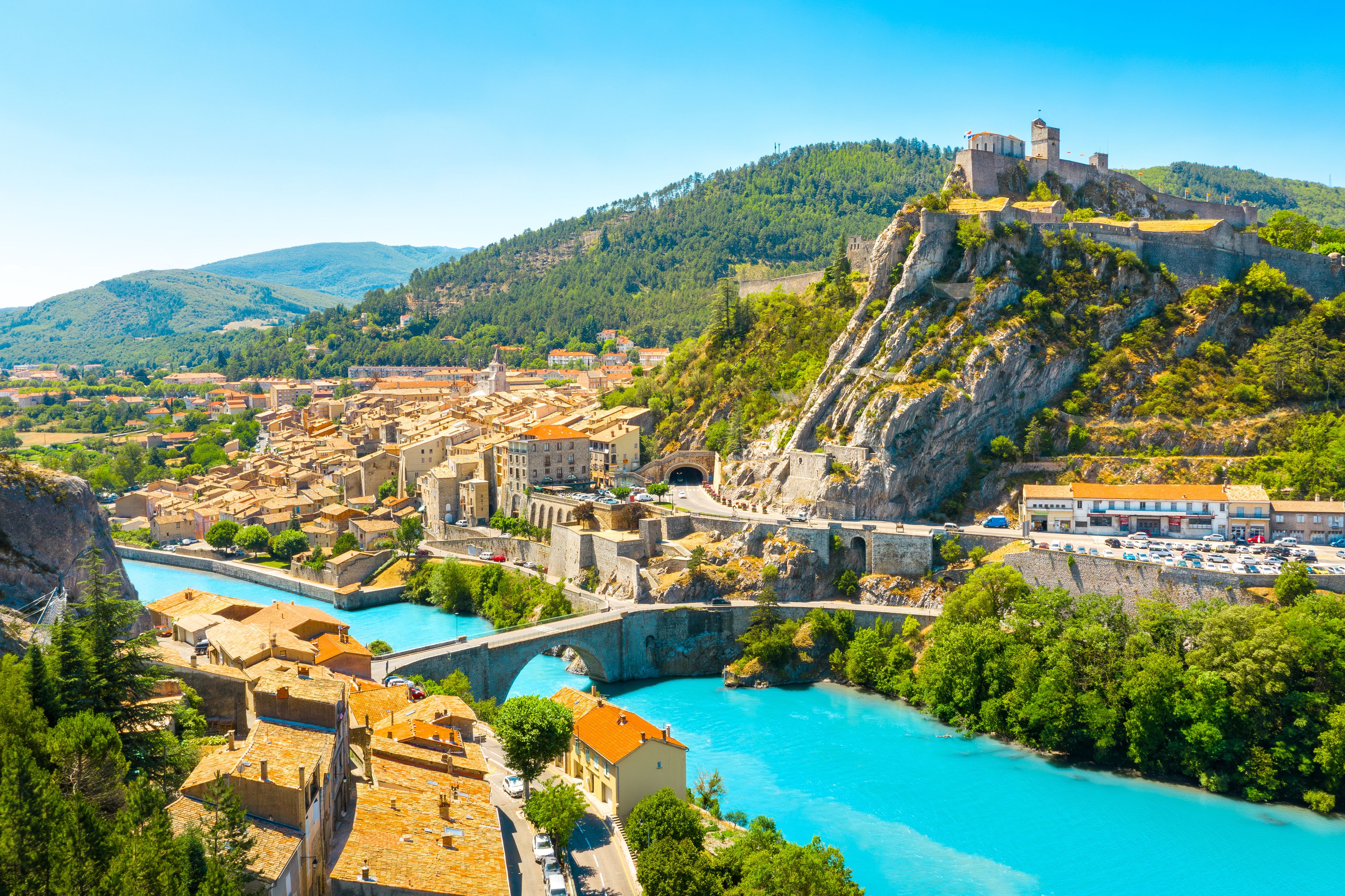 Eine Küstenstadt mit einer historischen Burg auf einem Hügel, einem Fluss und umgebender Natur.