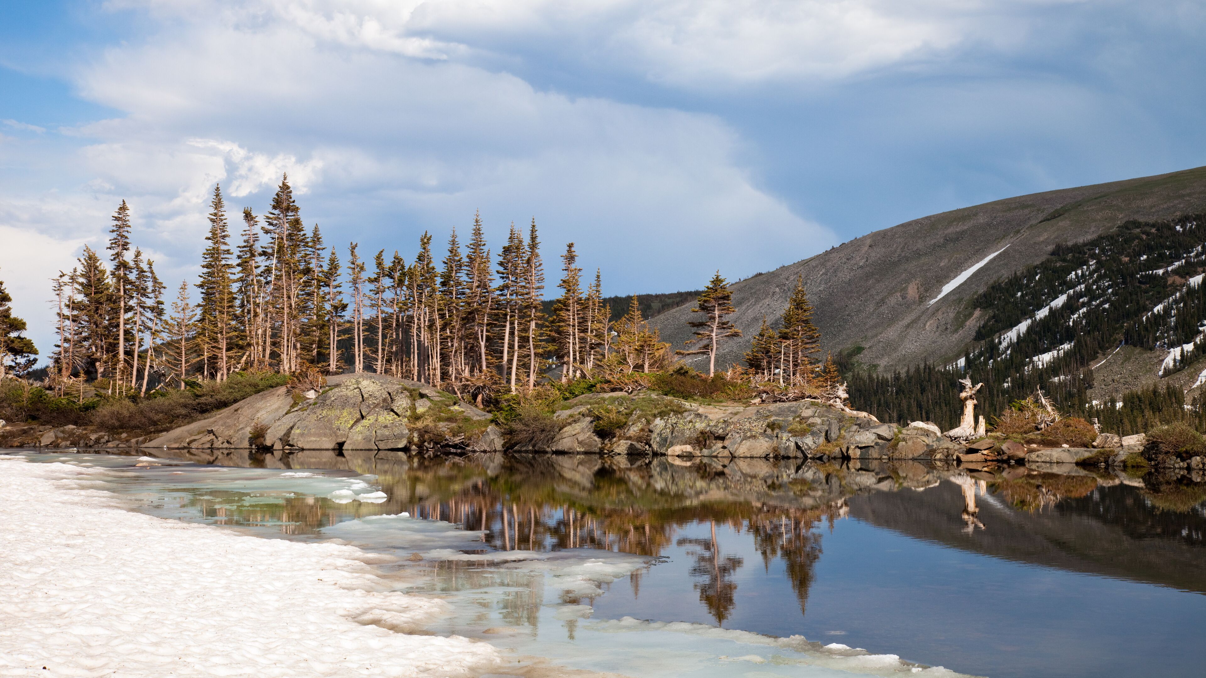 A calm lake with reflections of trees and a snow-covered shore.