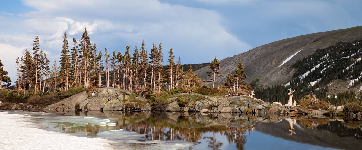 A calm lake with reflections of trees and a snow-covered shore.