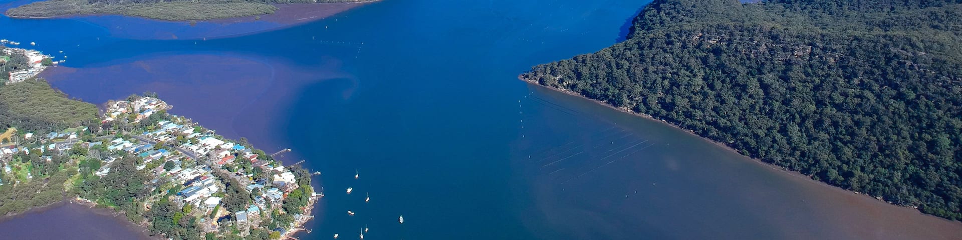 An aerial view of a coastal area with a bridge connecting two landmasses, surrounded by dense forests and clear blue waters.