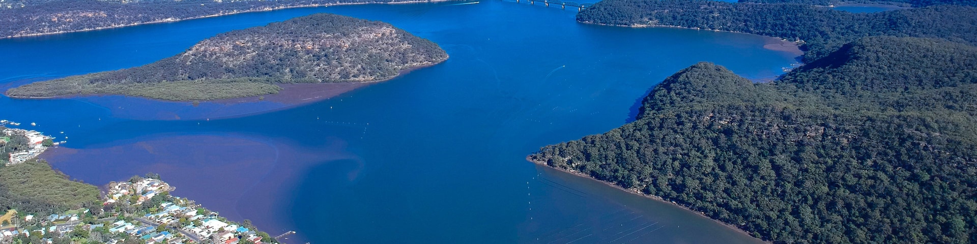 An aerial view of a coastal area with a bridge connecting two landmasses, surrounded by dense forests and clear blue waters.