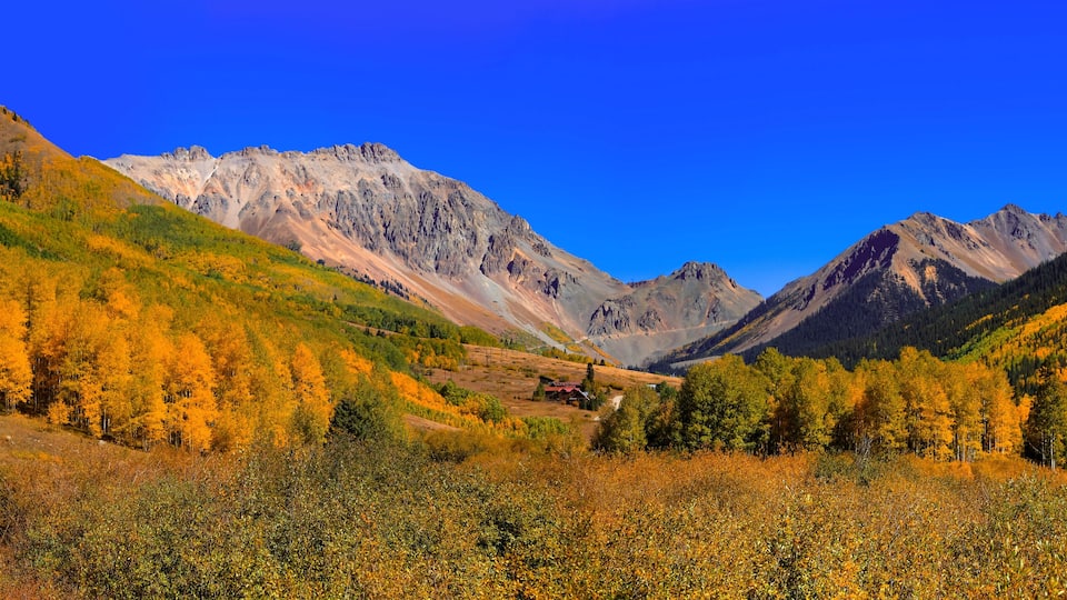 A mountainous landscape with autumn foliage, a dirt road, and a small cabin.