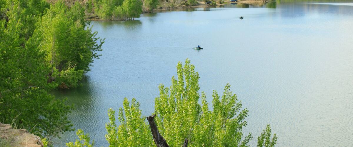 A serene lake surrounded by green vegetation and mountains in the background.