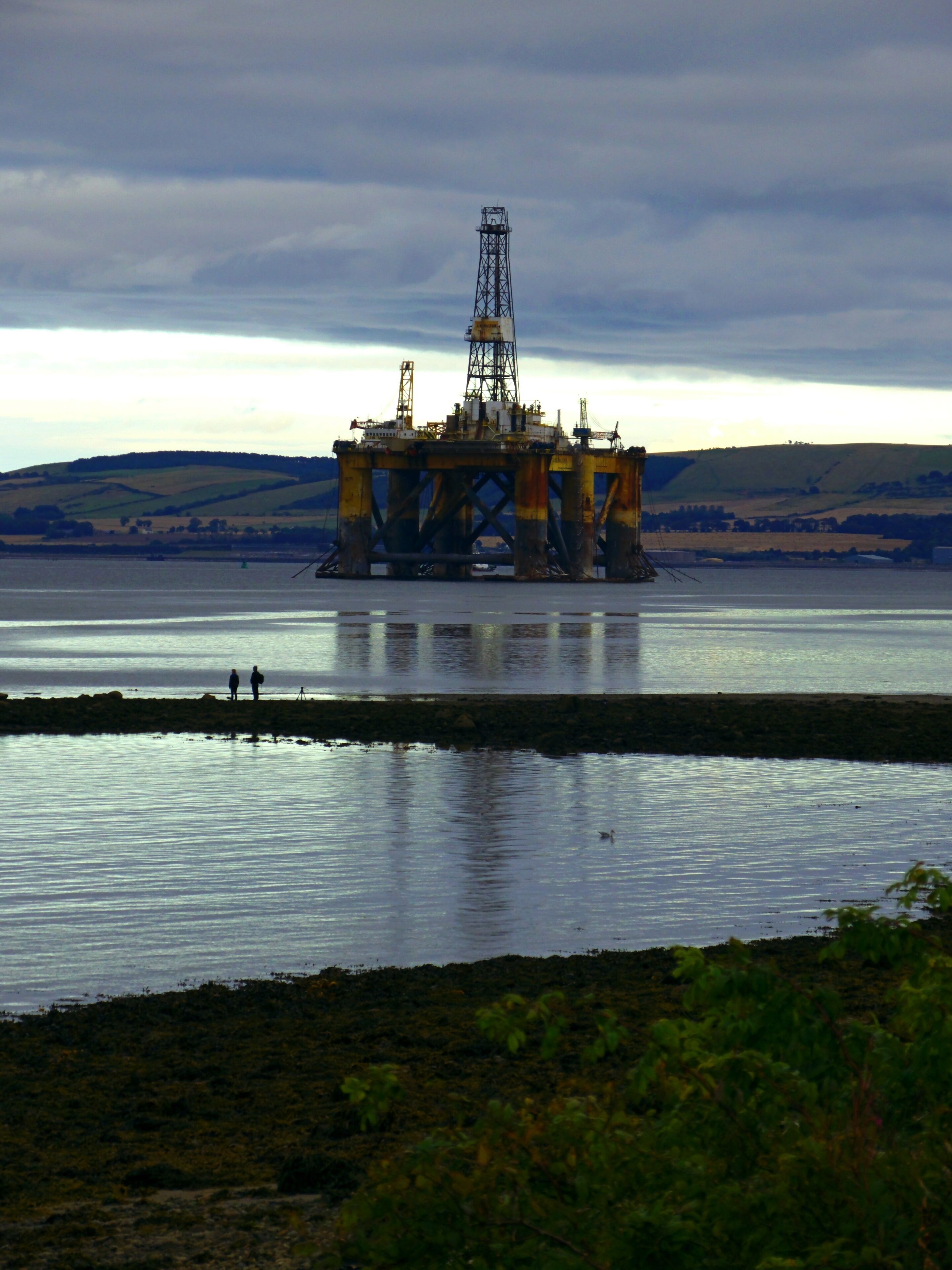 An offshore oil platform in a body of water with a cloudy sky.