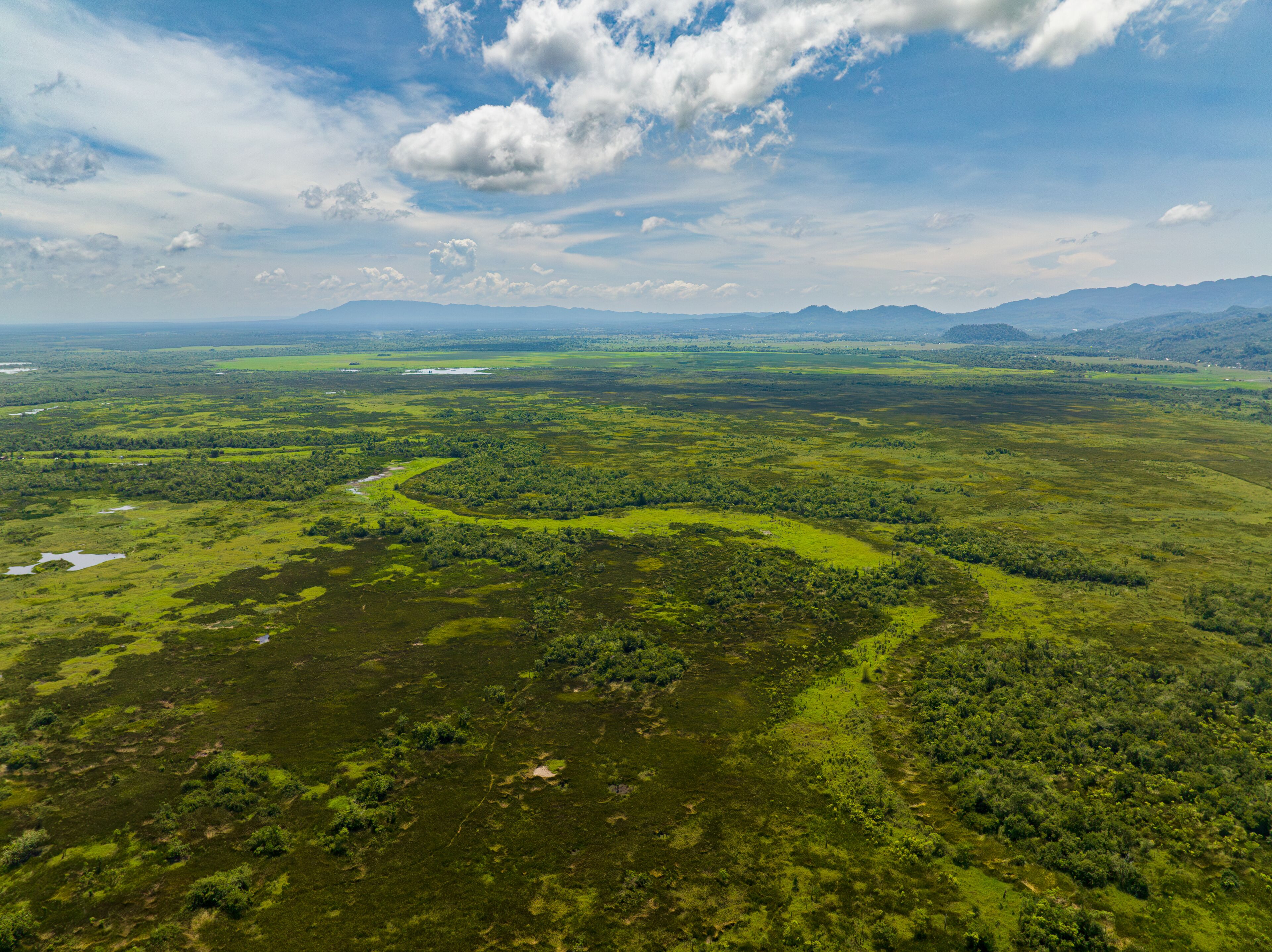 A vast landscape with a river winding through a green valley, surrounded by hills and mountains under a partly cloudy sky.