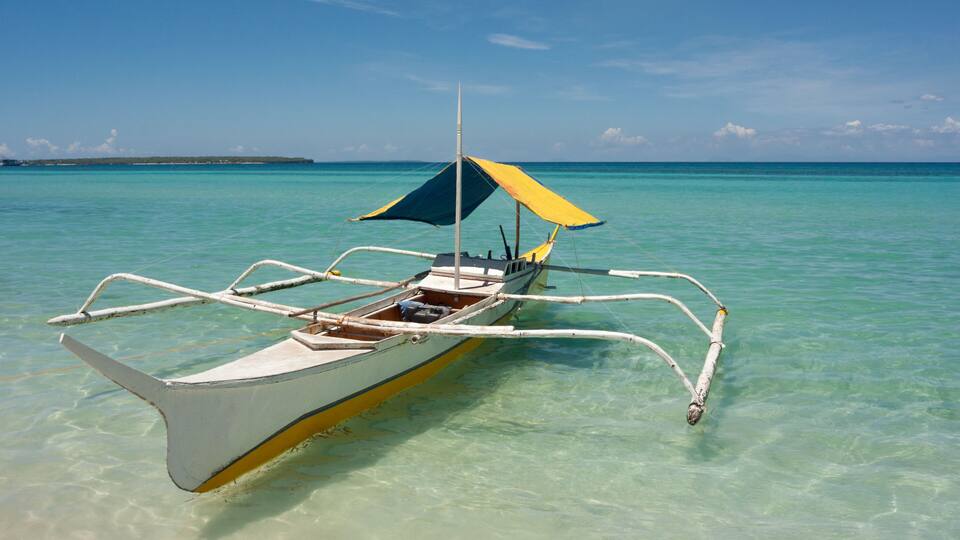 A traditional boat with a canopy, anchored in clear turquoise waters.