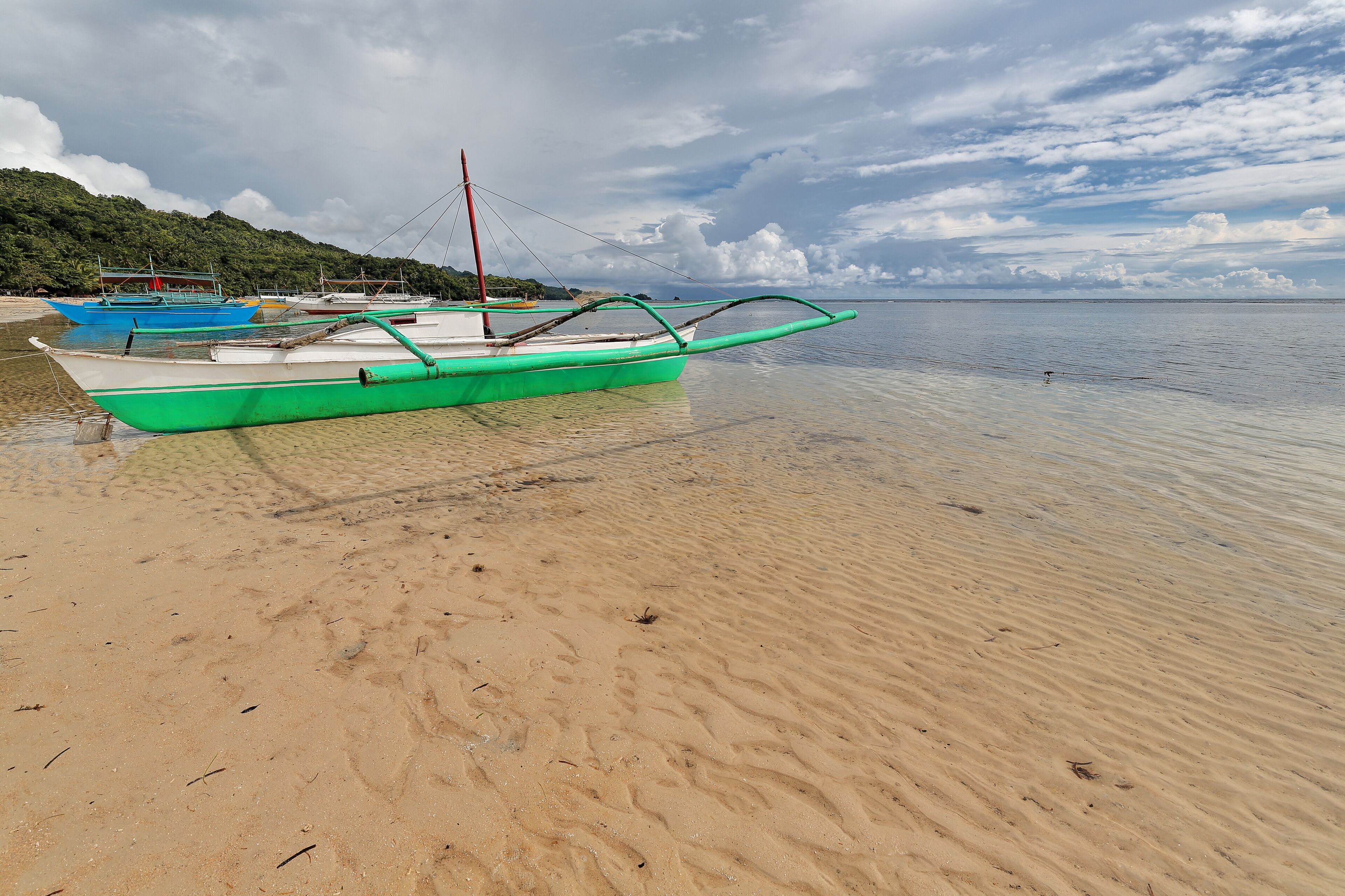 A beach with several boats, clear water, and a cloudy sky.