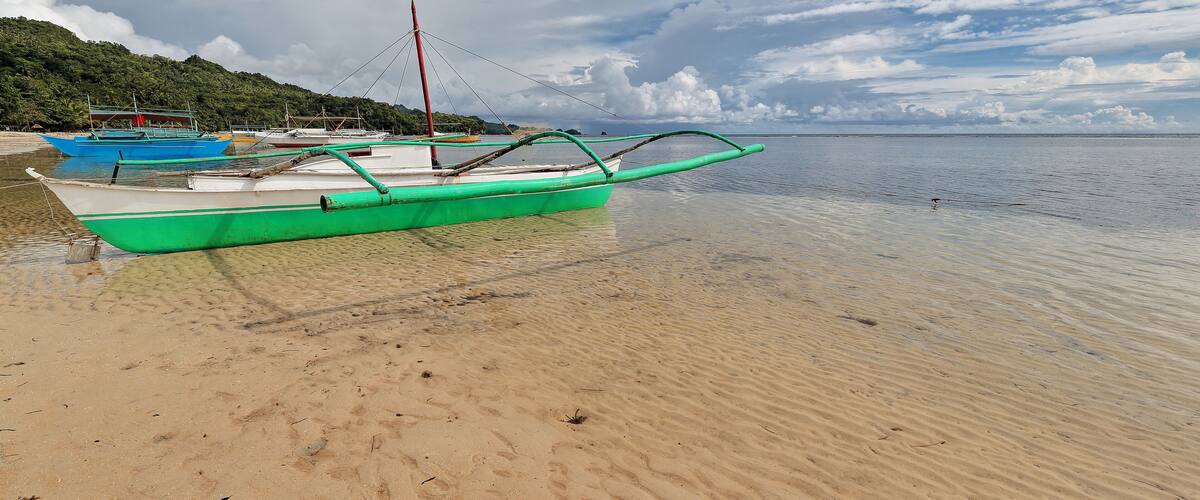 A beach with several boats, clear water, and a cloudy sky.