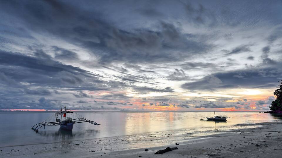 A boat on a calm sea with a cloudy sky and a sunset.