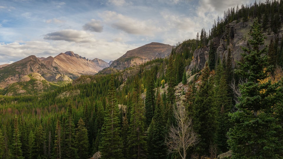 A mountainous landscape with dense forests and rocky peaks under a partly cloudy sky.