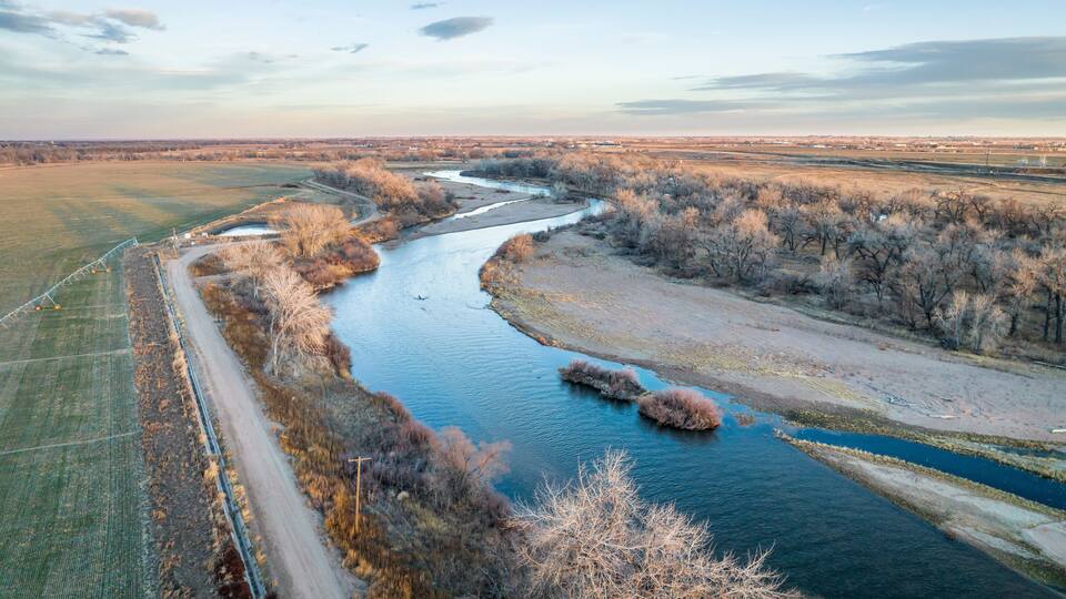 A river winding through a rural landscape with fields and sparse trees.