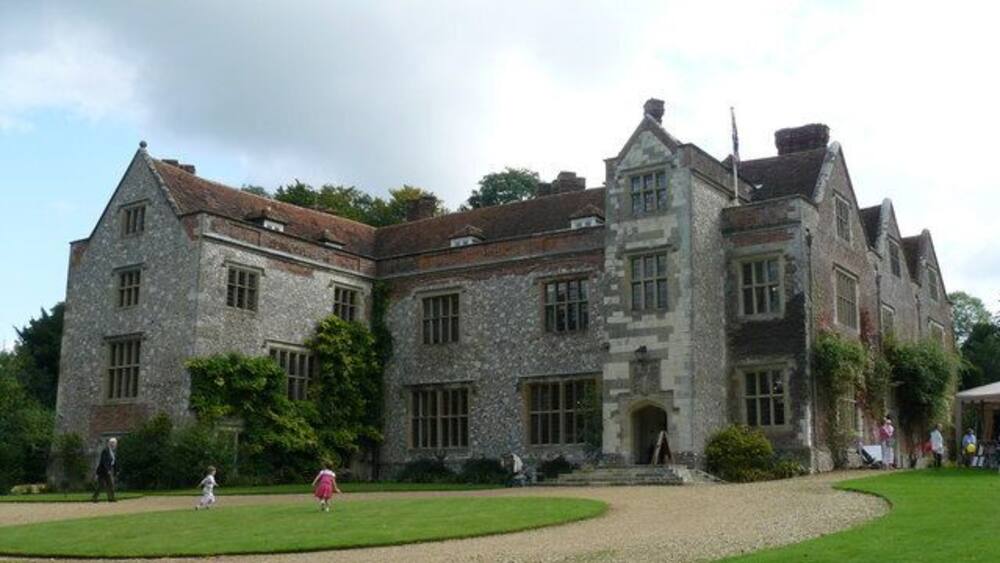A large stone building with a formal garden and a flagpole.
