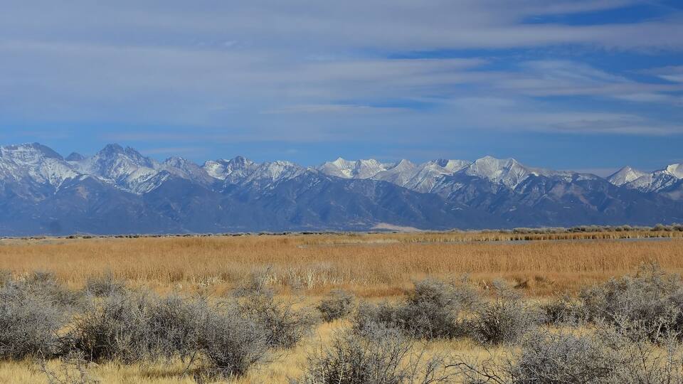 A mountain range with snow-capped peaks and a flat, grassy plain in the foreground.