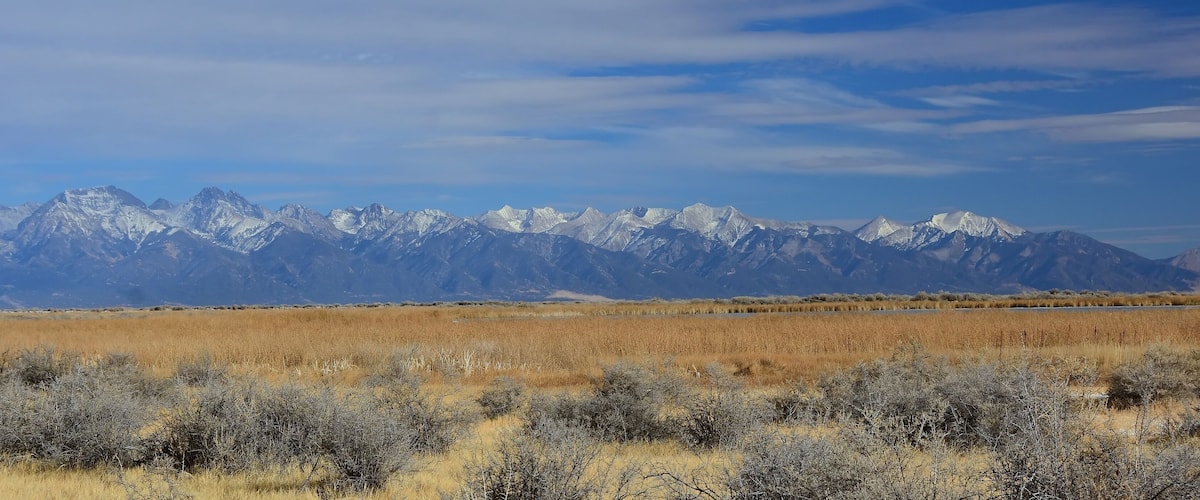 A mountain range with snow-capped peaks and a flat, grassy plain in the foreground.