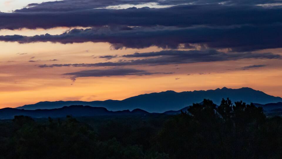 A mountain range at sunset with clouds reflecting the sky's colors.