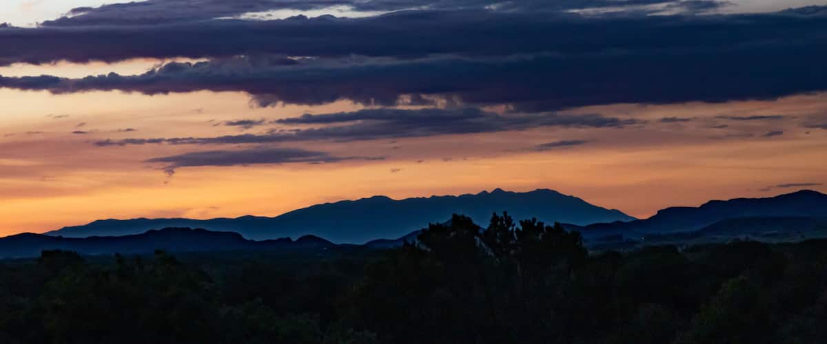 A mountain range at sunset with clouds reflecting the sky's colors.