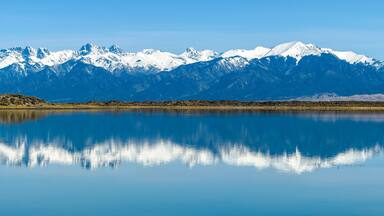 A calm lake reflecting snow-capped mountains under a clear sky.
