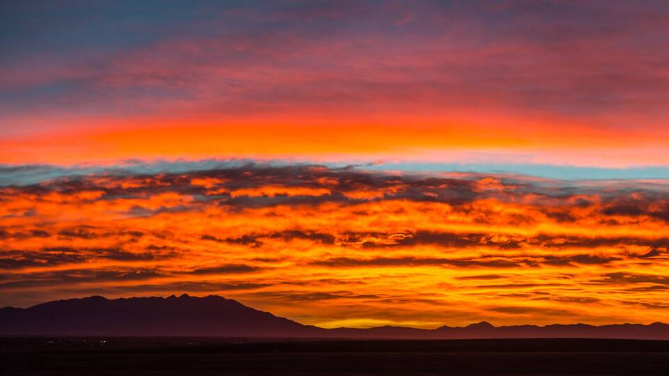 A sunset over a mountain range with vibrant orange and red clouds.