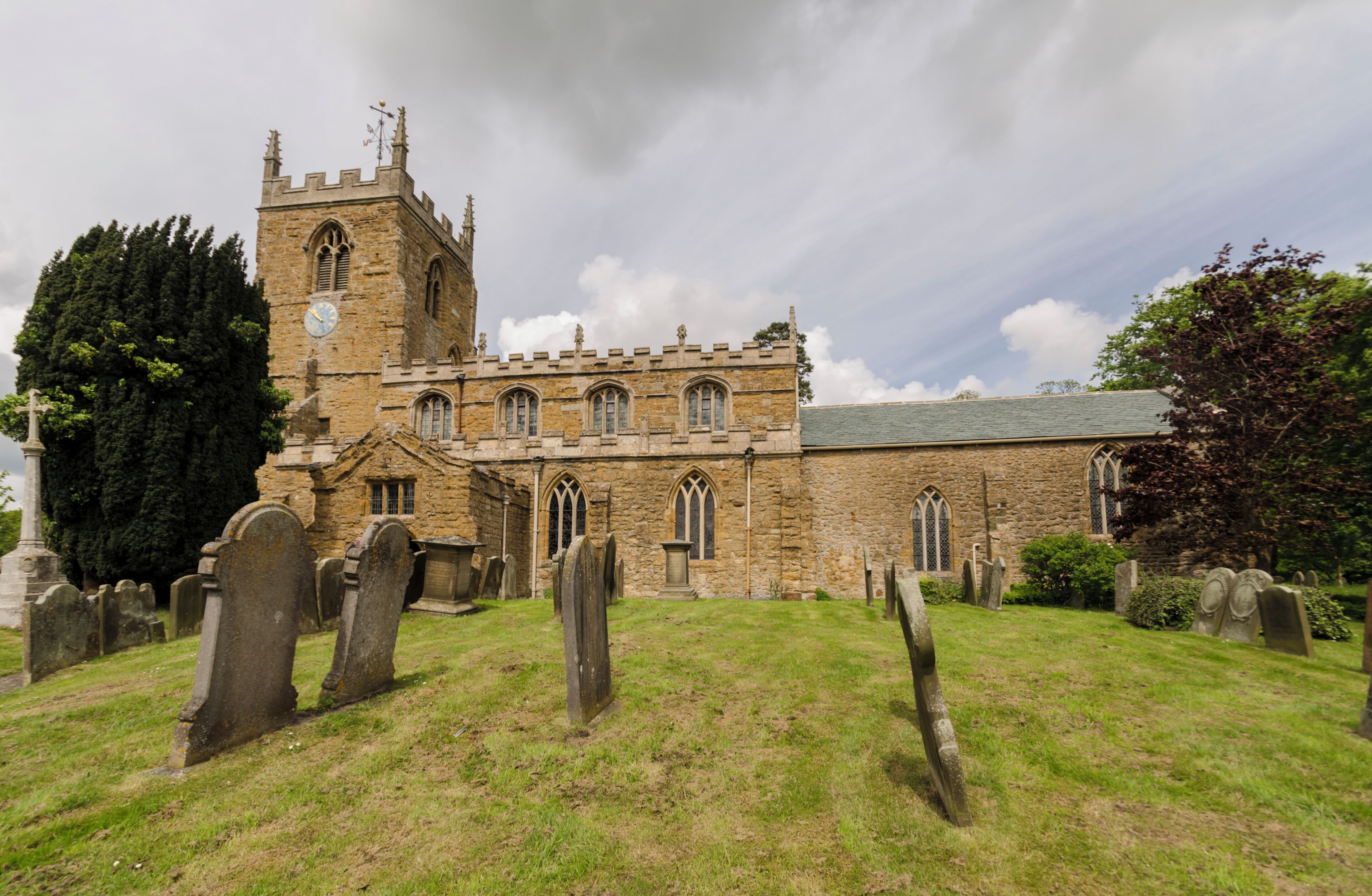 A historic church with a tall tower and multiple arched windows, surrounded by a cemetery with headstones.