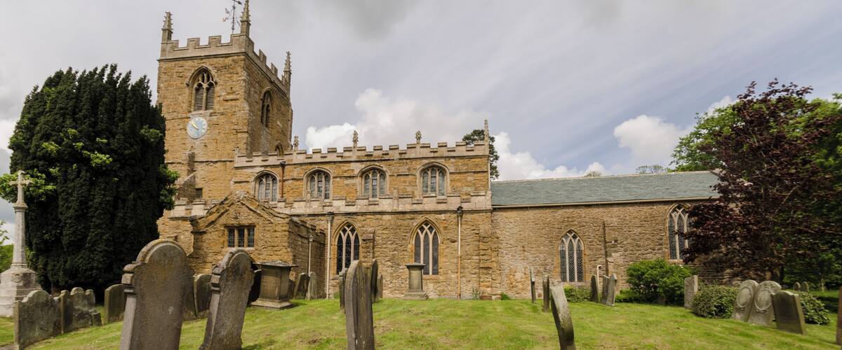 A historic church with a tall tower and multiple arched windows, surrounded by a cemetery with headstones.