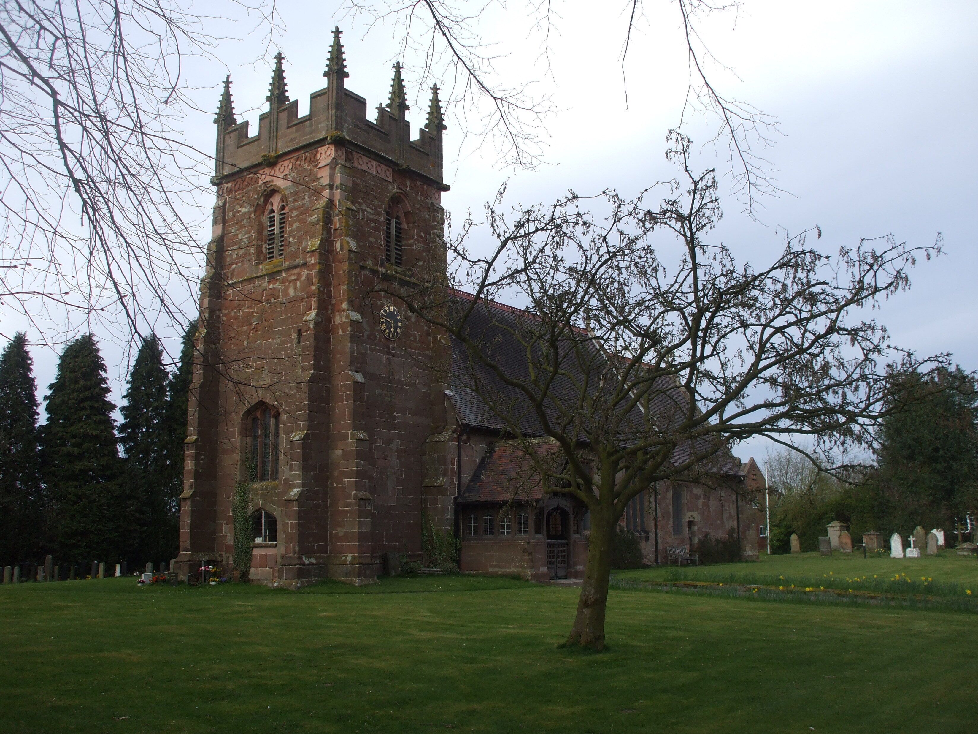 A historic church with a tall tower and a large tree in the foreground.
