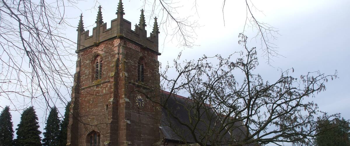 A historic church with a tall tower and a large tree in the foreground.