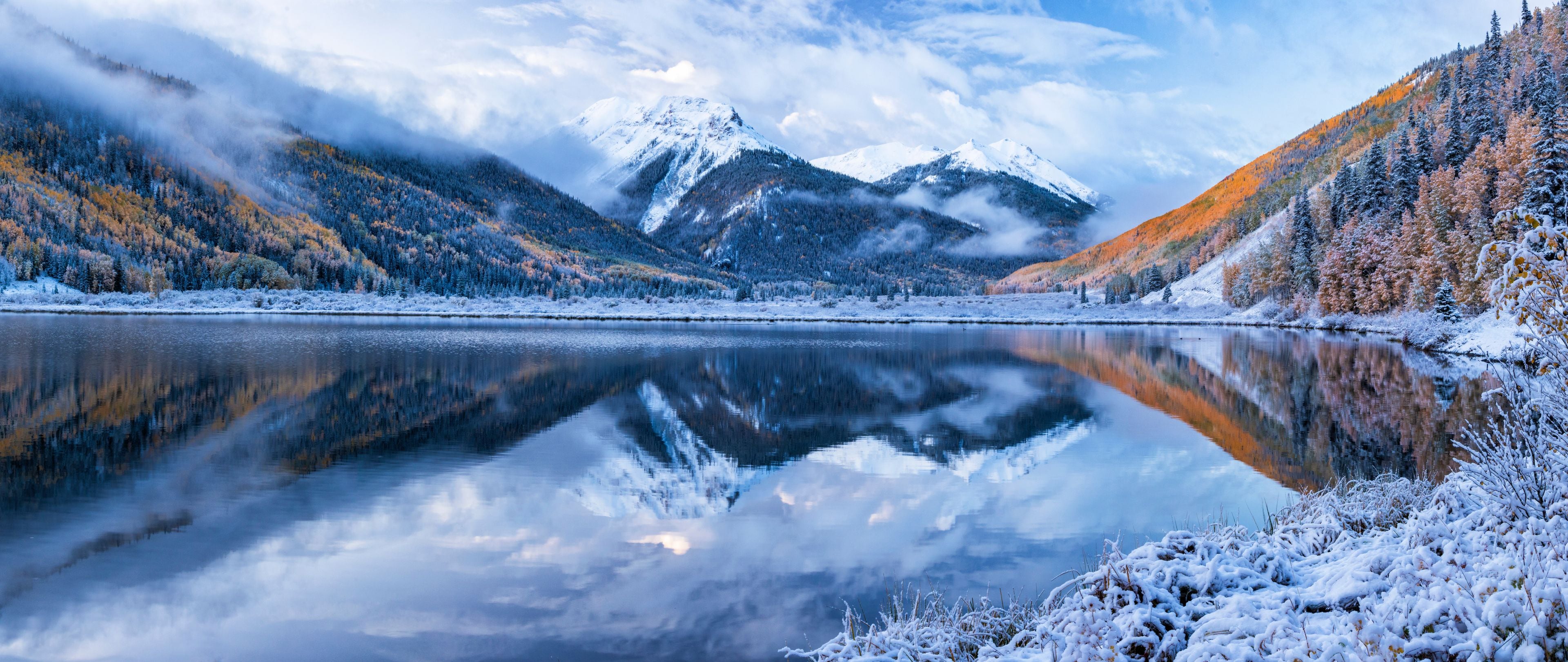 A serene mountain lake with snow-covered trees and mountains in the background.