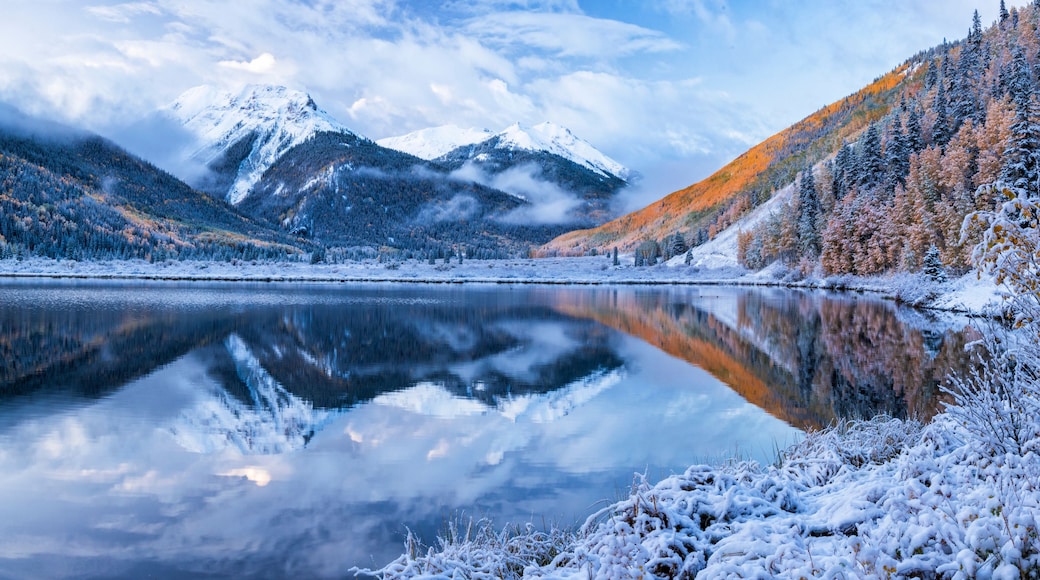 Ein friedlicher Bergsee mit schneebedeckten Bäumen und Bergen im Hintergrund.