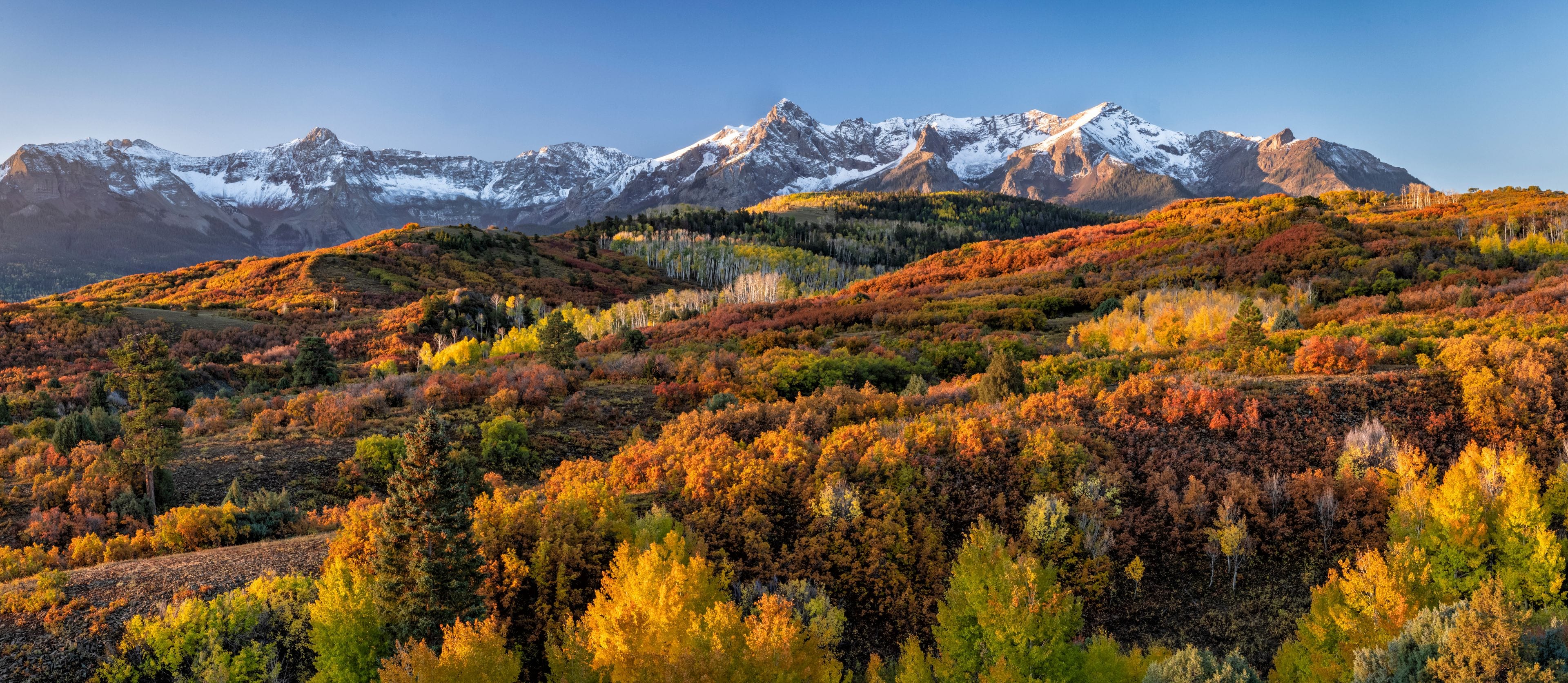 A mountainous landscape with autumn foliage and snow-capped peaks.