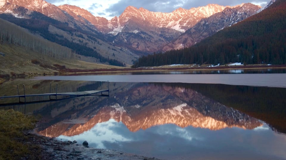 A mountain lake with reflections of the mountains and a wooden bridge.