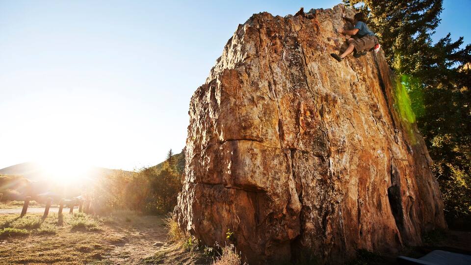 A person rock climbing a large, rugged rock formation with a forest in the background.