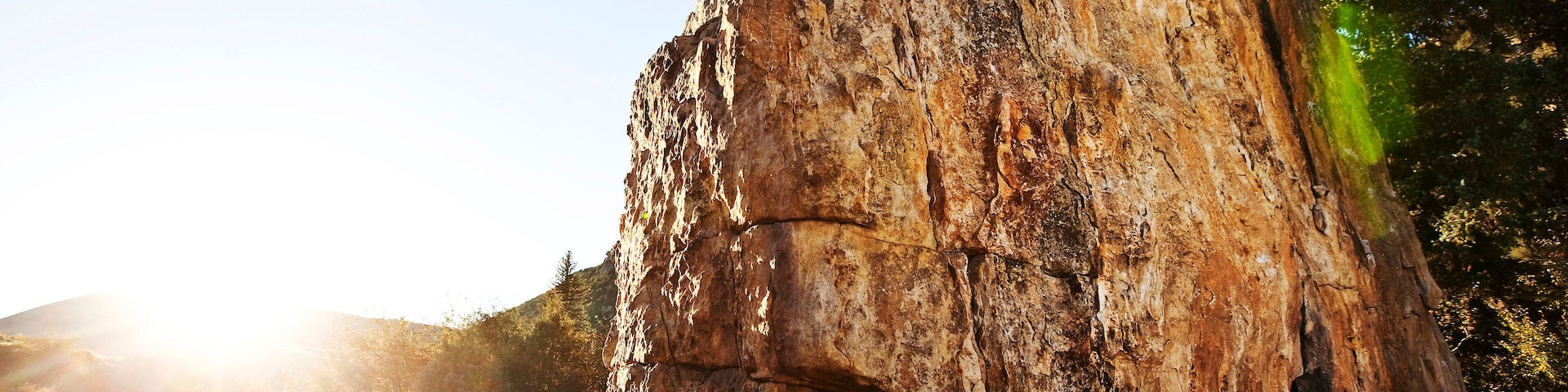 Uma pessoa escalando uma grande e acidentada formação rochosa, com uma floresta ao fundo.