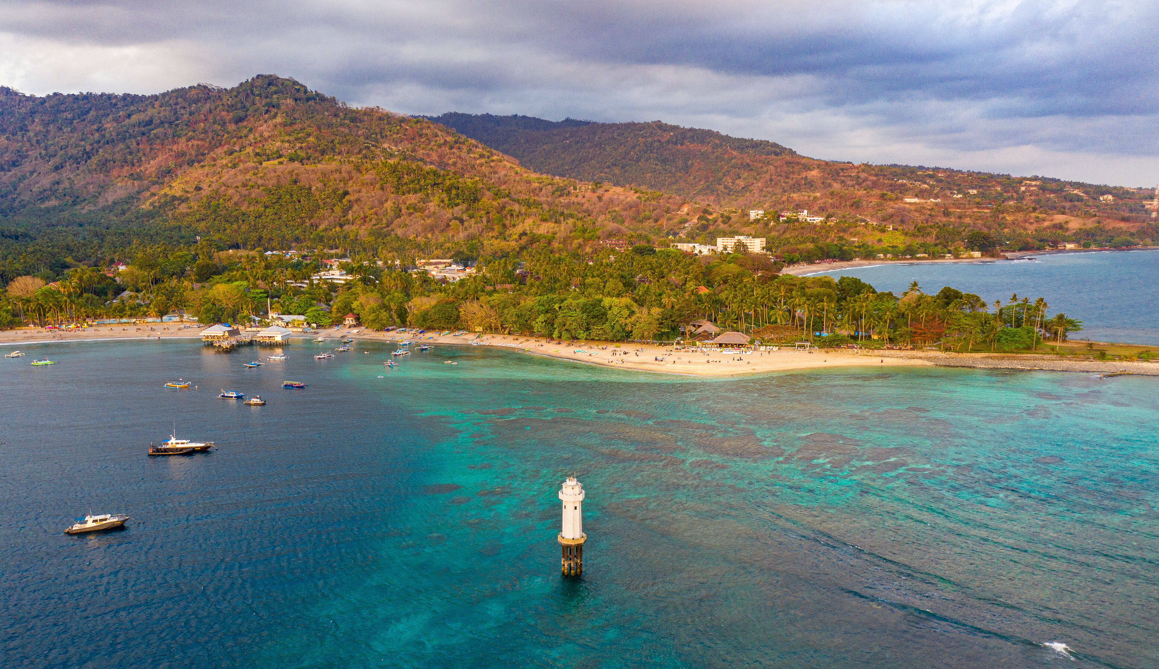 A coastal town with a lighthouse, clear turquoise waters, and a beach.