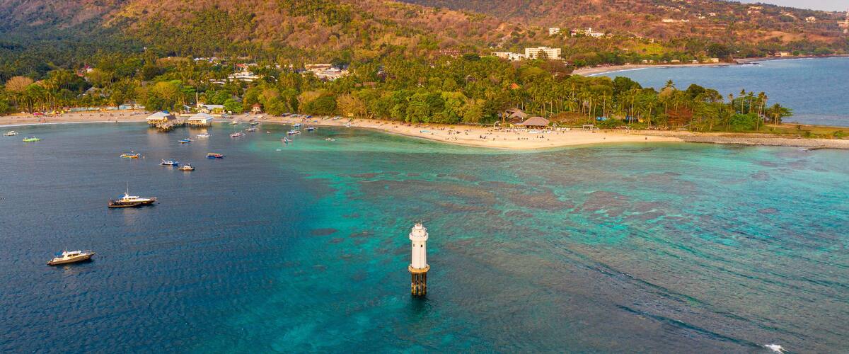 A coastal town with a lighthouse, clear turquoise waters, and a beach.
