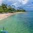 A clear turquoise sea, a sandy beach, and palm trees under a blue sky.
