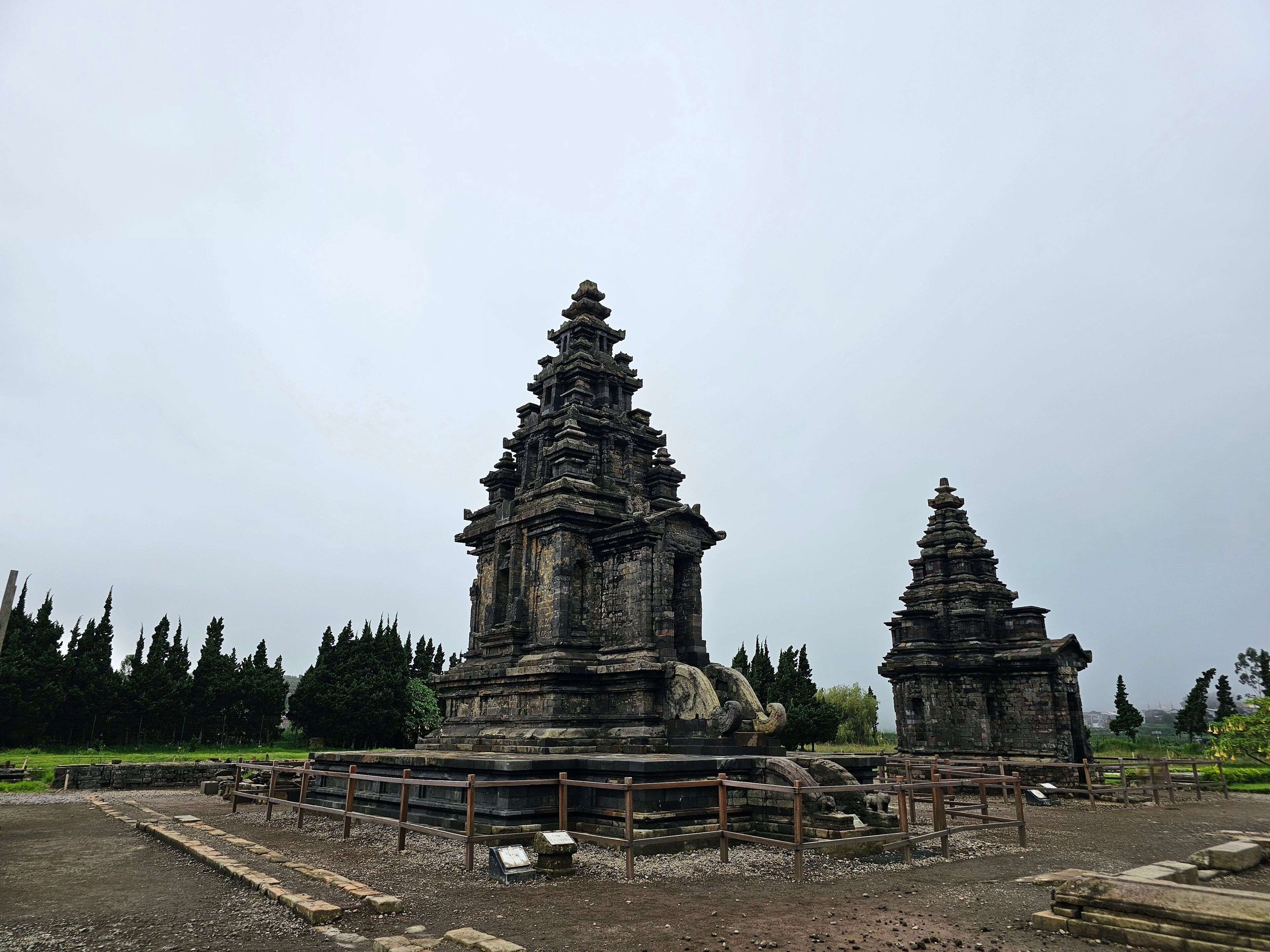 Ancient stone structures with intricate carvings, surrounded by a gravel path and wooden railings.