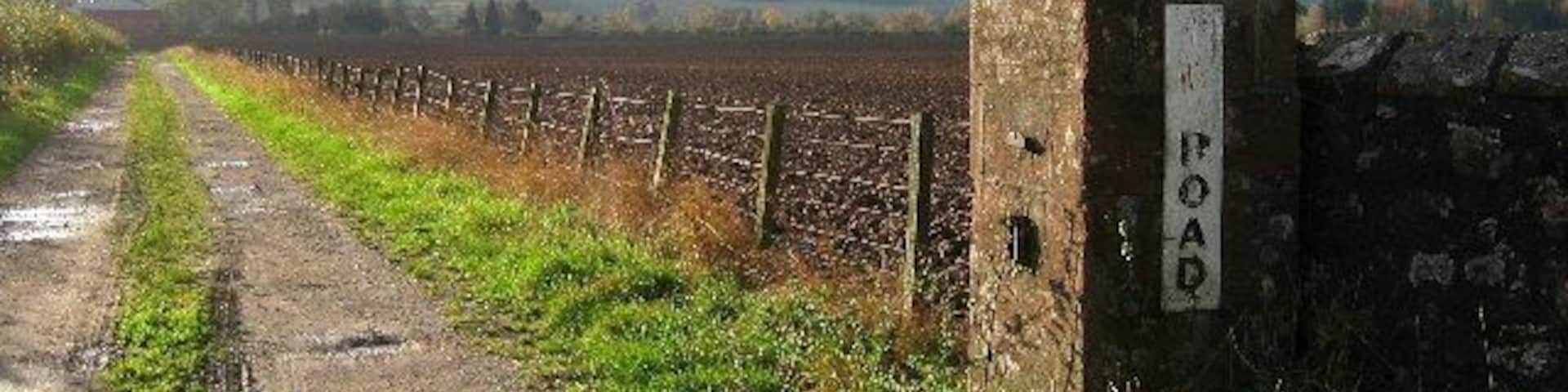 A rural dirt road with a stone marker labeled "ROAD" and a fence running alongside it.