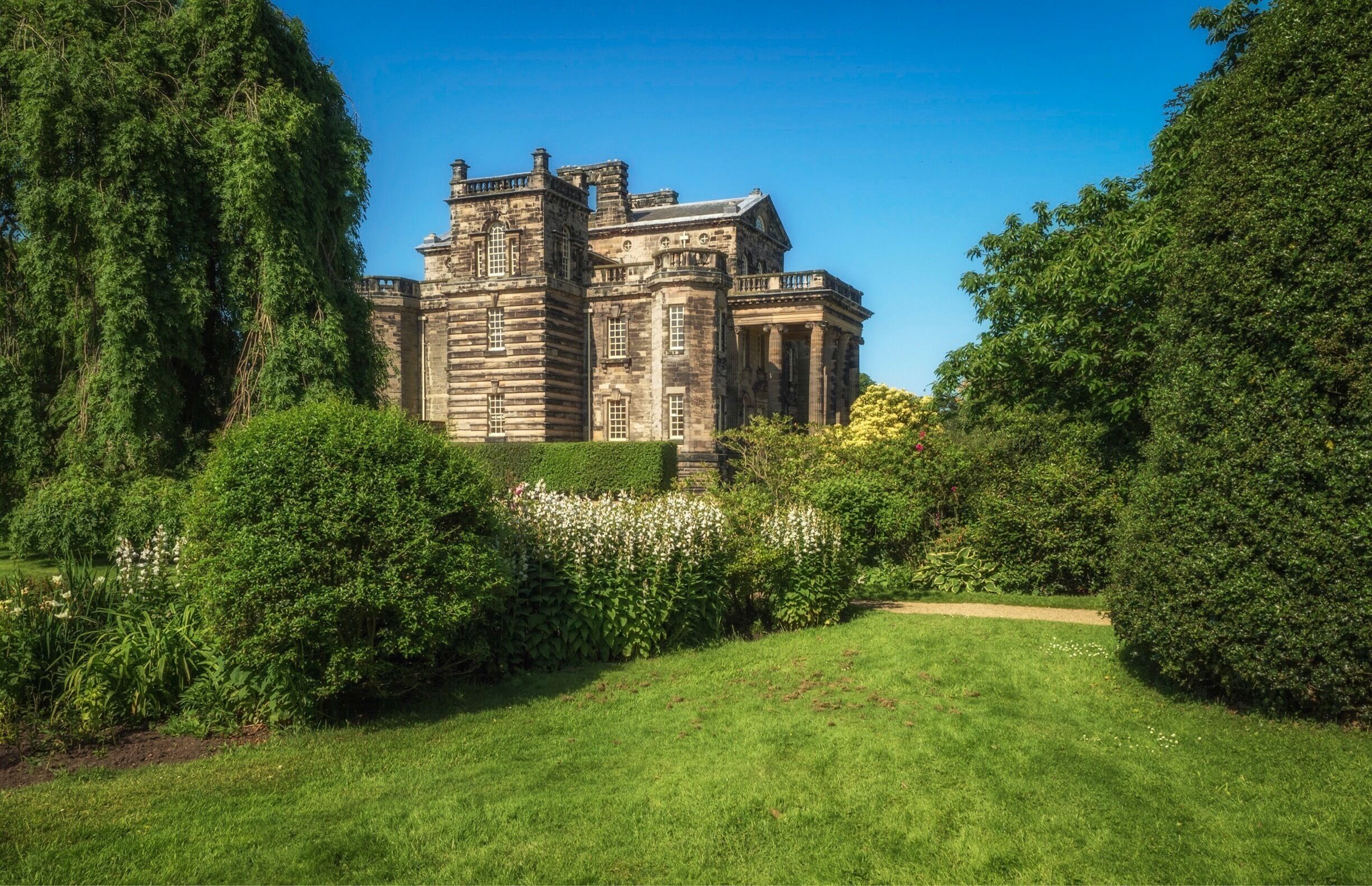 A historic stone building surrounded by lush greenery and a well-maintained lawn.