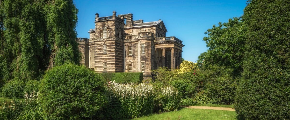 A historic stone building surrounded by lush greenery and a well-maintained lawn.