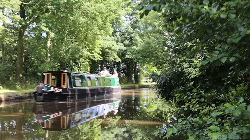 A narrowboat on a calm river surrounded by dense greenery.