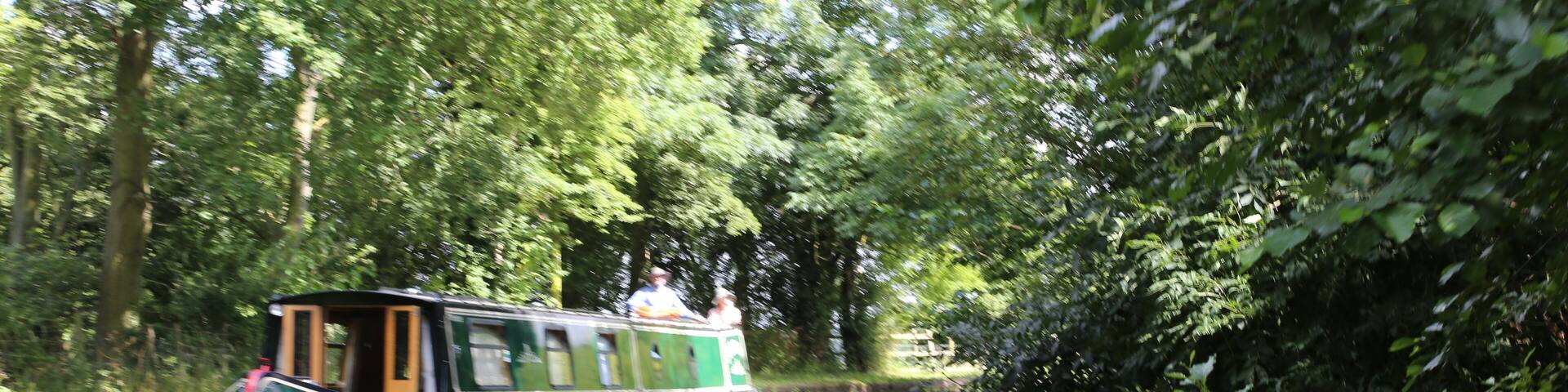 A narrowboat on a calm river surrounded by dense greenery.